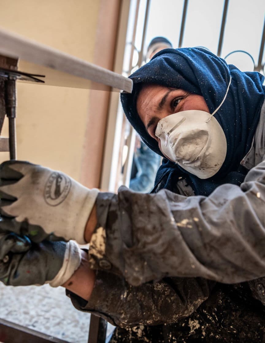 Una mujer con velo, máscara y guantes de obra trabaja en un proyecto de construcción en el Iraq.