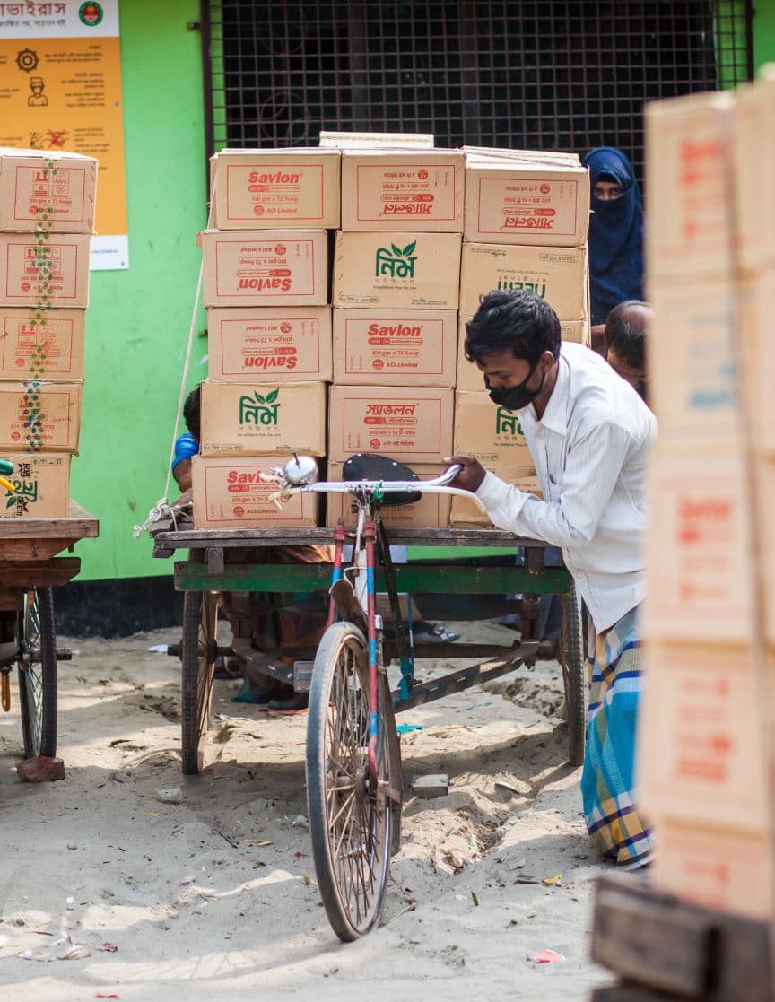 Un hombre empuja una bicicleta cargada de cajas por una calle de Bangladesh.