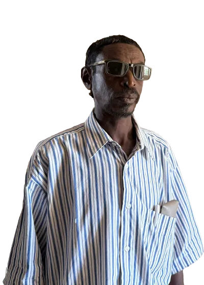 Man in sunglasses and a striped shirt. He has a calm expression, with a pocket square visible in his shirt.