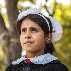 Portrait d'une jeune fille portant un bandeau blanc, avec des arbres en arrière-plan.