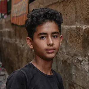 Retrato de un niño en un callejón estrecho, con una pared de ladrillos en el fondo.