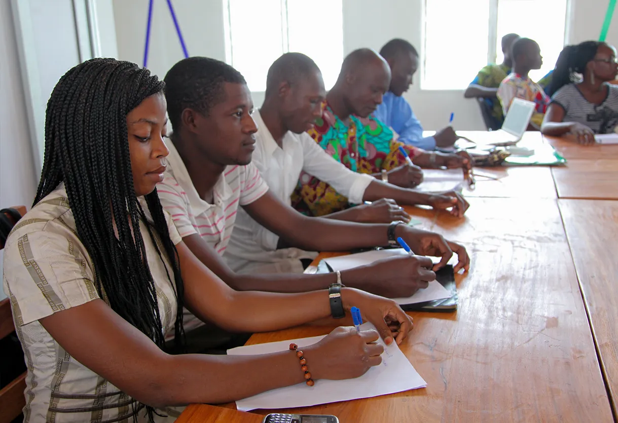 Several people gathered around a table, focused on writing and sharing ideas in a collaborative environment.