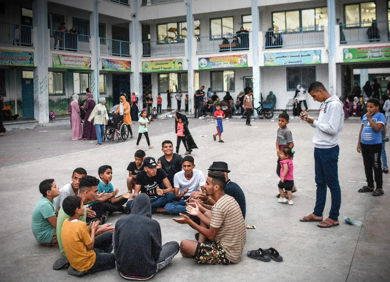 A group of individuals seated on the ground, gathered in front of a large building, engaged in conversation.