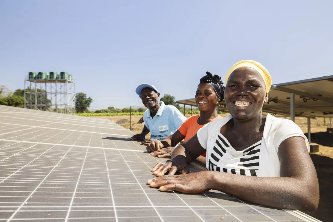 Tres personas están junto a una gran instalación de paneles solares.