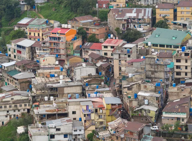 Densely packed, multi-storey houses cover a hillside, many with blue water tanks on their roofs.