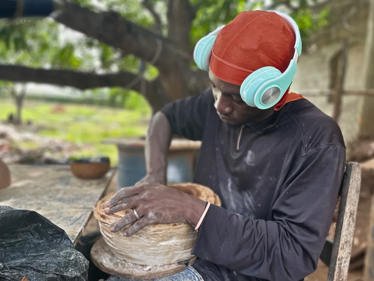 Close up of a hand stirring thick brown clay in a shallow pit.