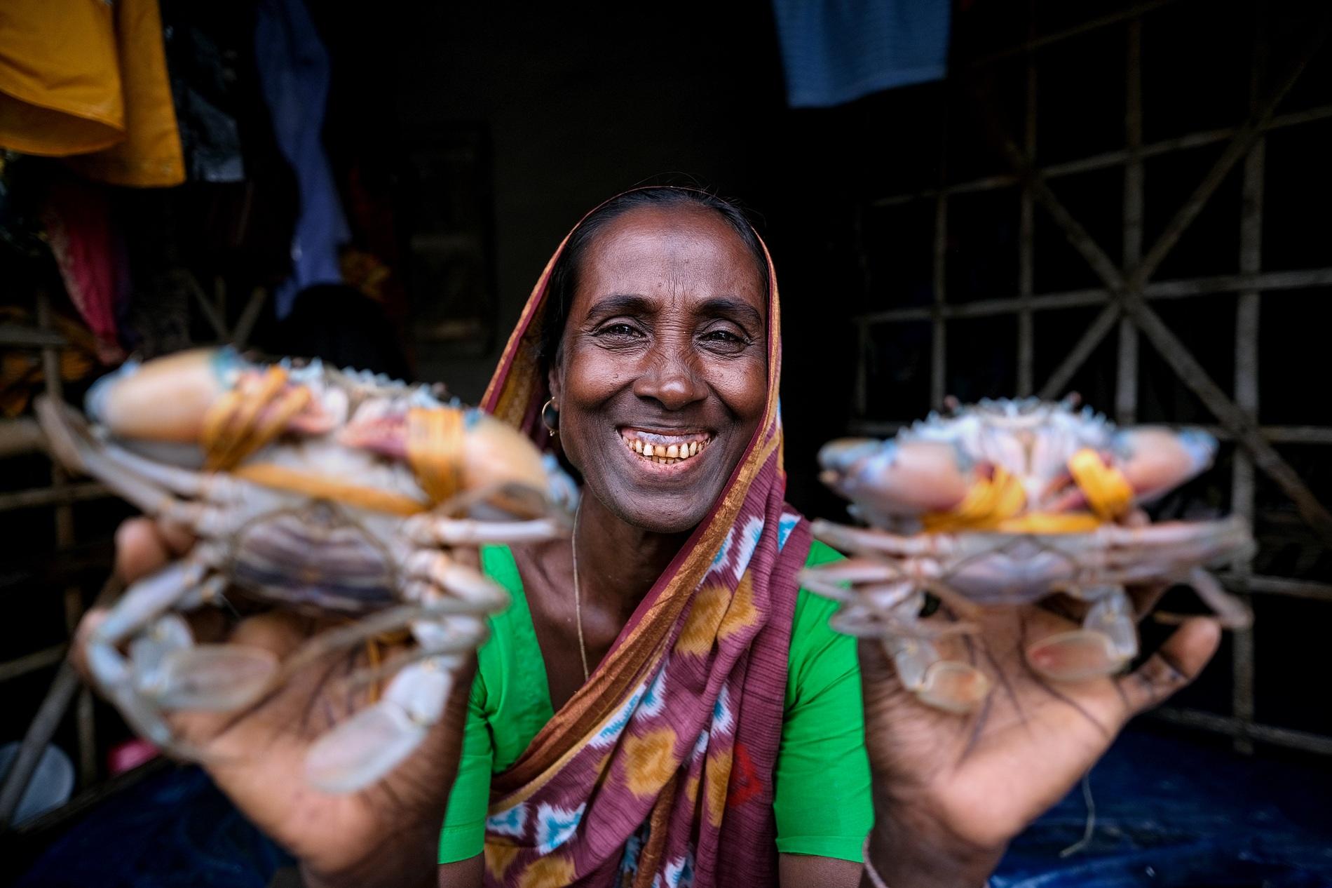 Smiling woman in a colourful sari holds two large crabs toward the camera.